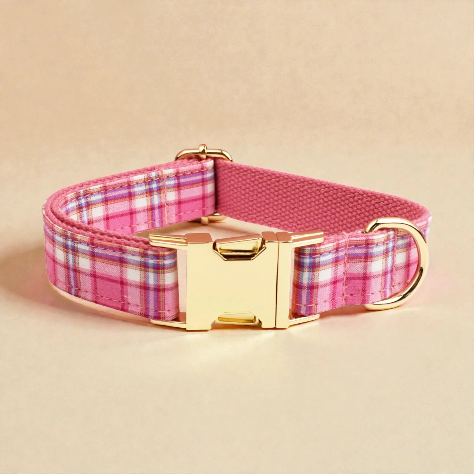Dog collar with pink plaid pattern and gold buckle on a beige background