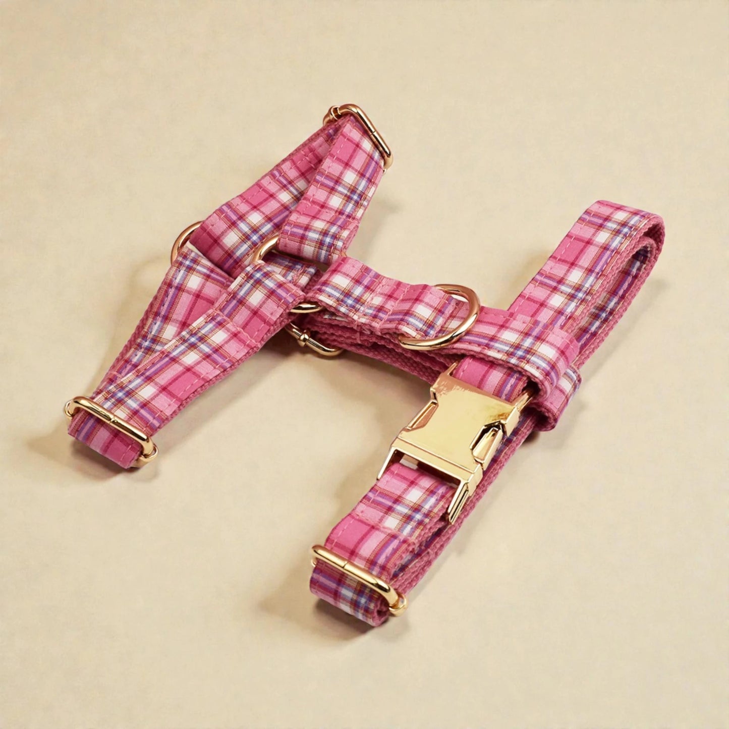 Pink plaid dog harness with gold hardware on a beige background