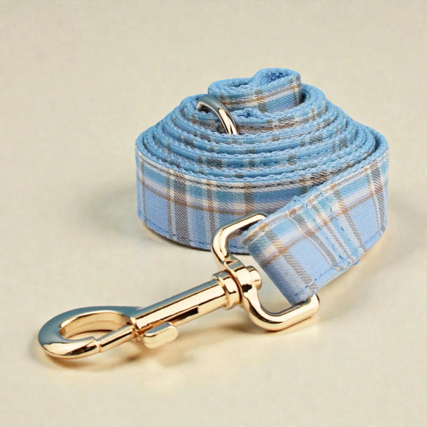 Blue plaid dog lead with gold hardware on a beige background