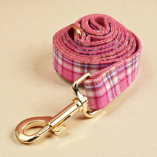 Pink plaid dog lead with gold clip on a beige background