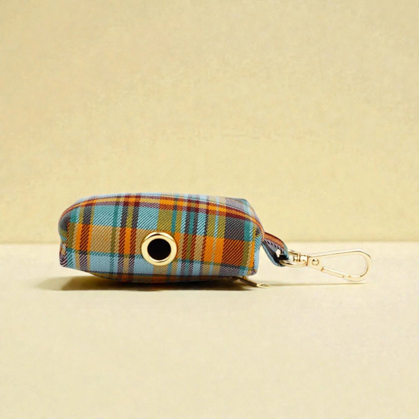 Plaid patterned dog poop bag holder with a clip on a beige background