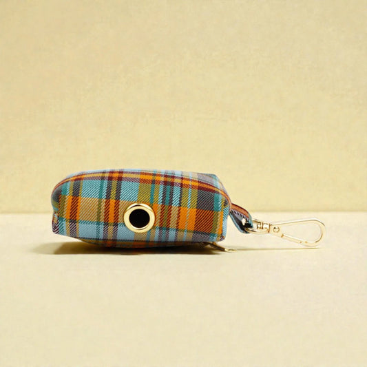 Plaid patterned dog poop bag holder with a clip on a beige background