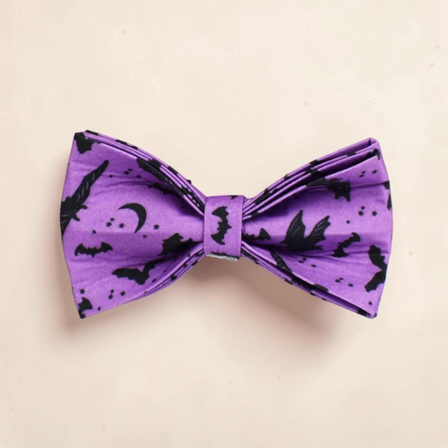 A purple dog bow tie with a black print of bats, moons and stars. Perfect for Halloween.