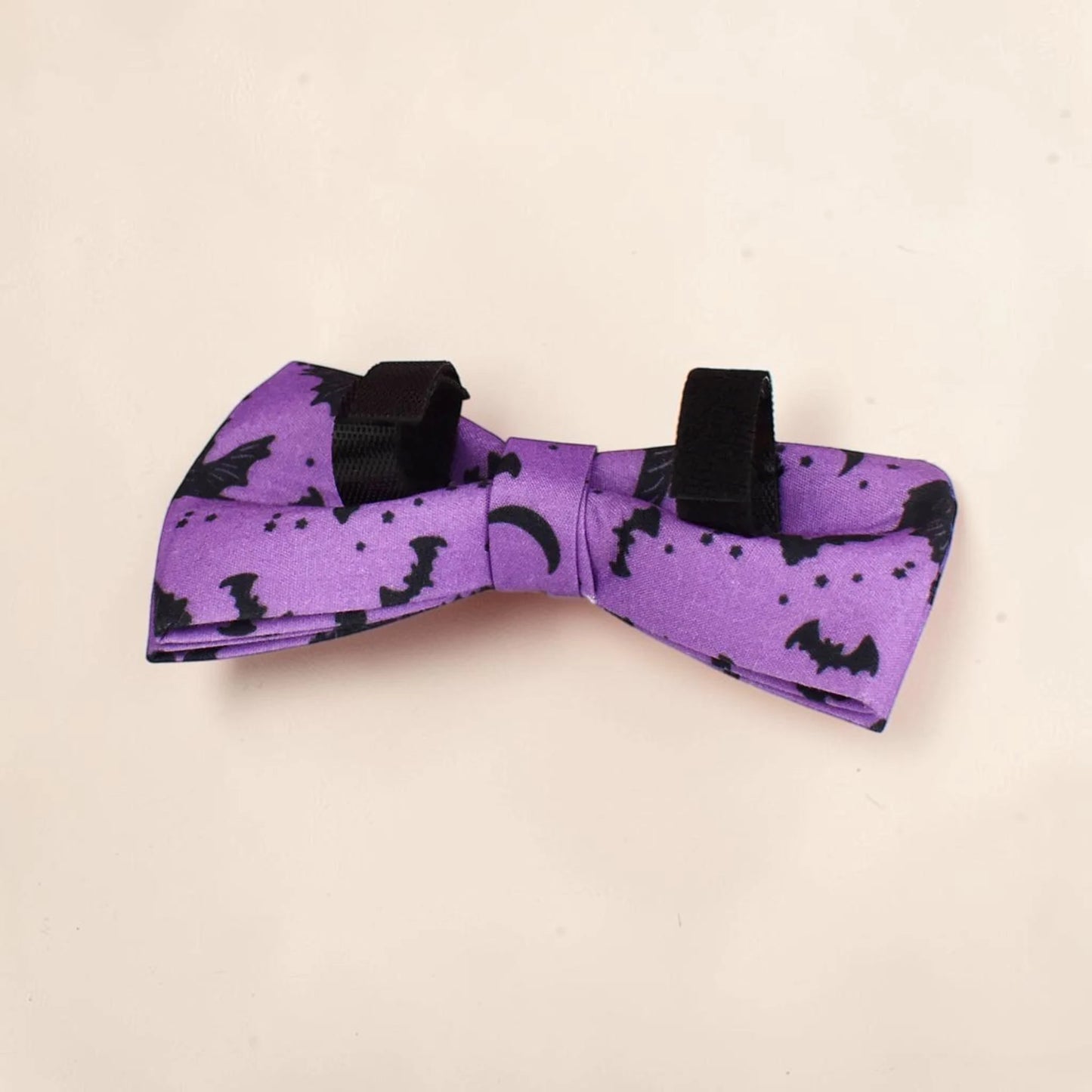 A purple detachable dog bow tie with a black print of bats, moons and stars. Perfect for Halloween.