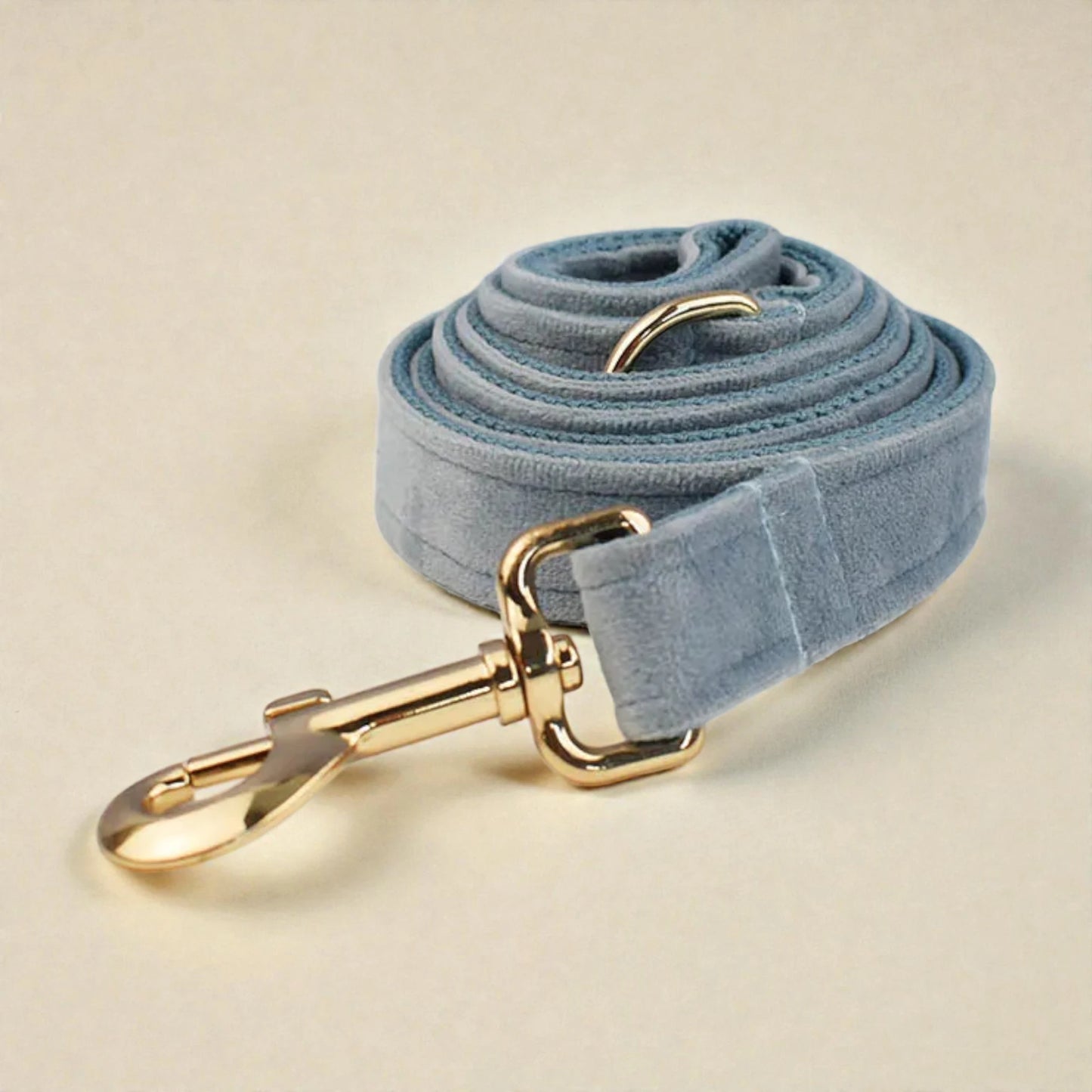 Light blue velvet dog leash with gold hardware on a beige background
