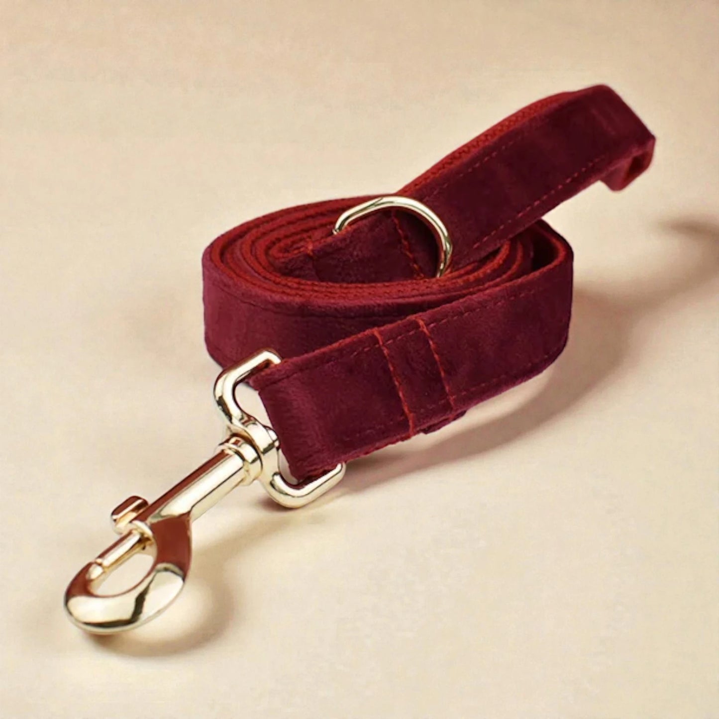 Red velvet dog lead with gold hardware on a beige background