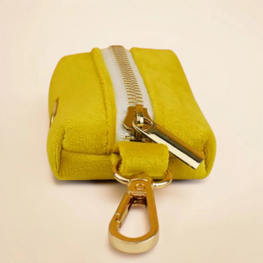 Yellow dog poop bag holder with a gold zip and clip on a beige background