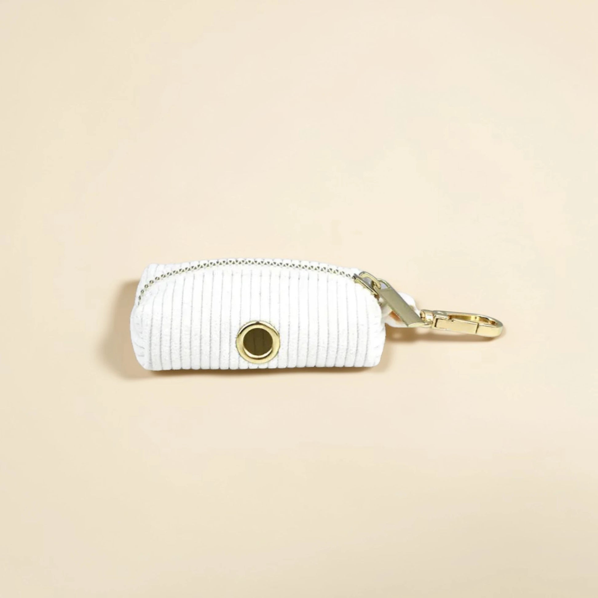 White corduroy dog poop bag holder with gold zip and clip on a beige background
