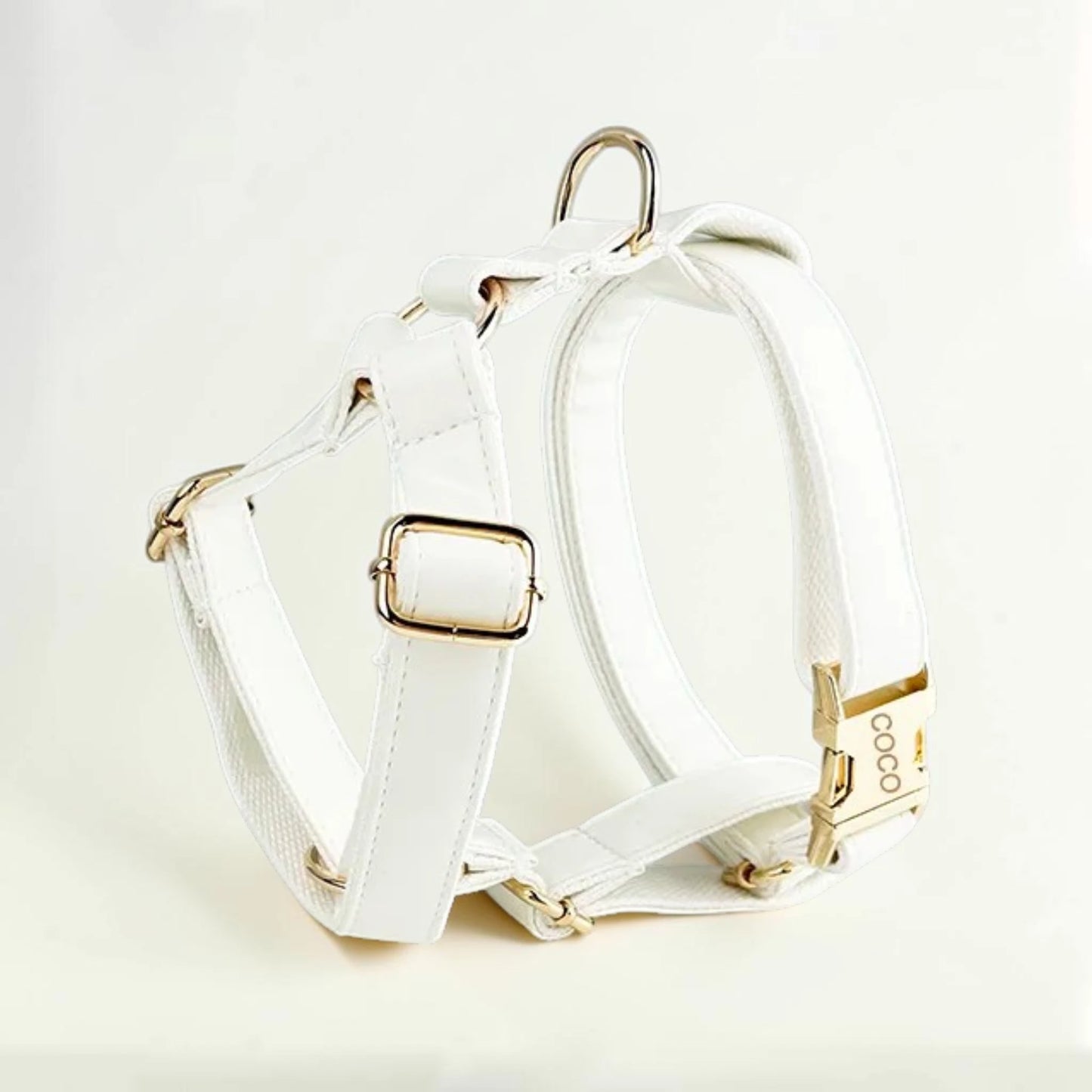 White dog harness with gold hardware on a light beige background