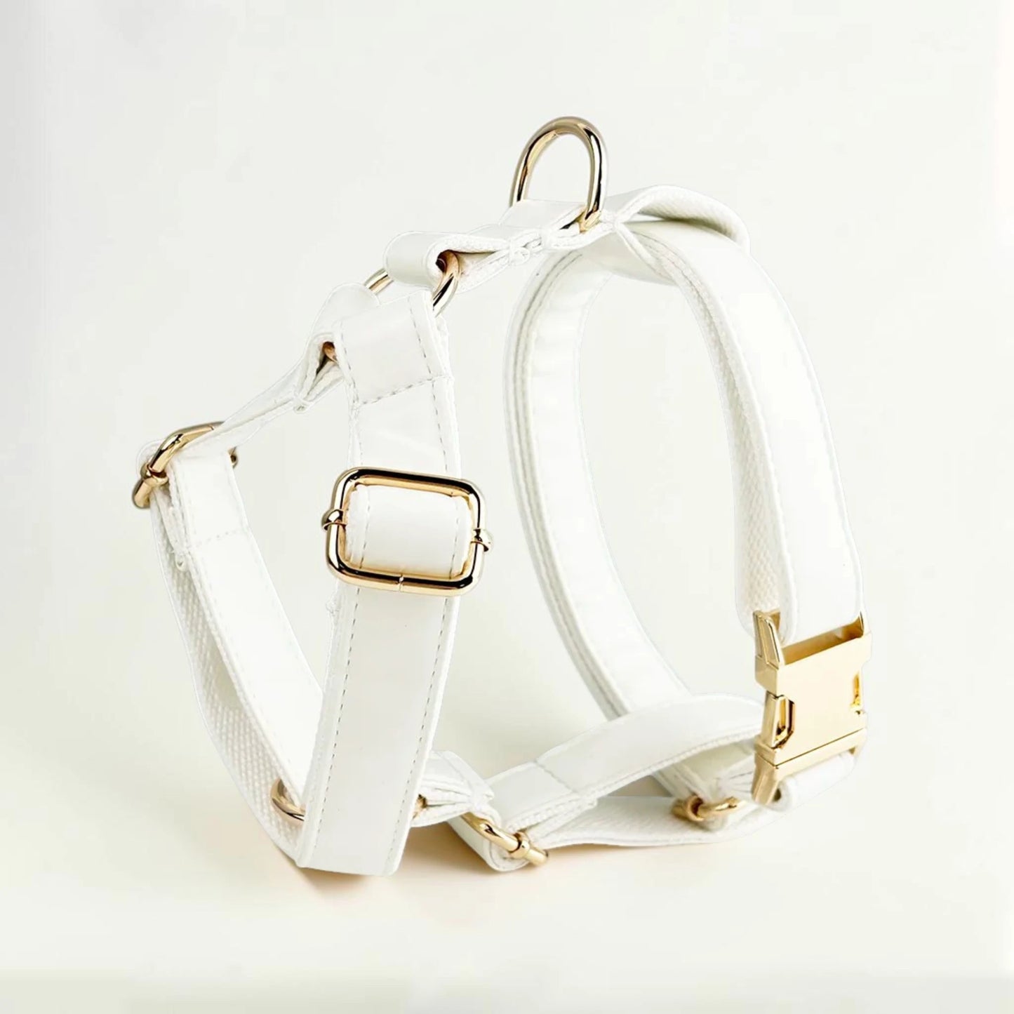 White dog harness with gold buckle on a light background