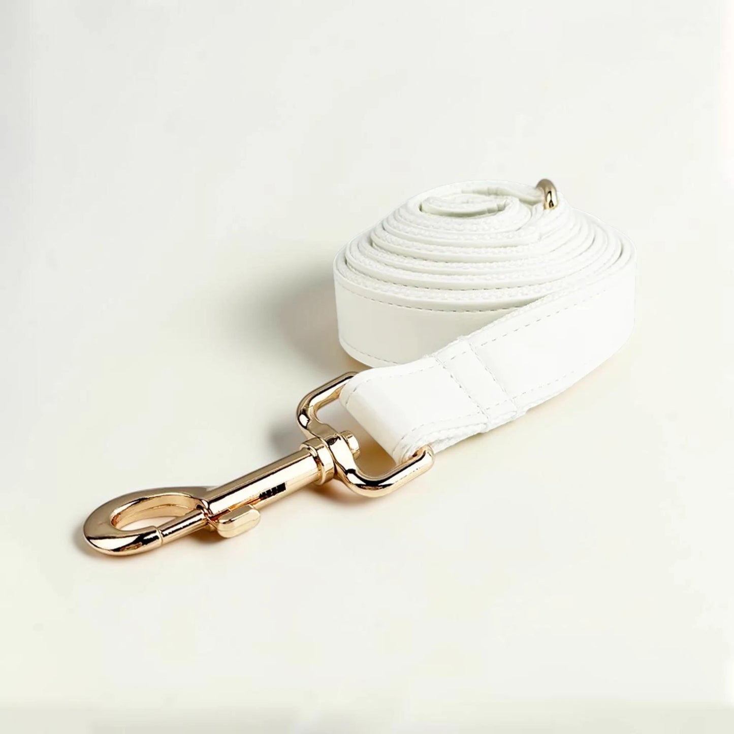 White faux leather dog lead with gold clip on a light beige background