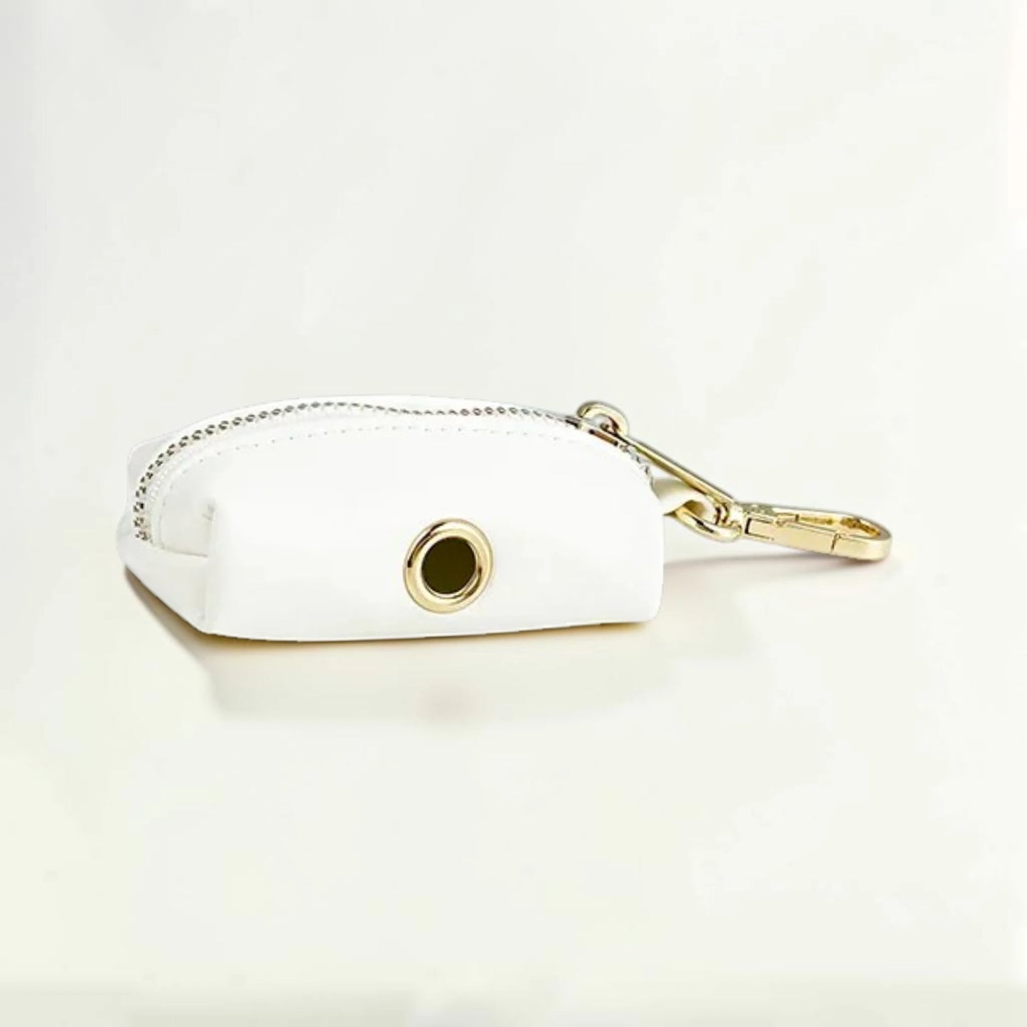 White faux leather dog poop bag holder with gold zip and clip on a light beige background