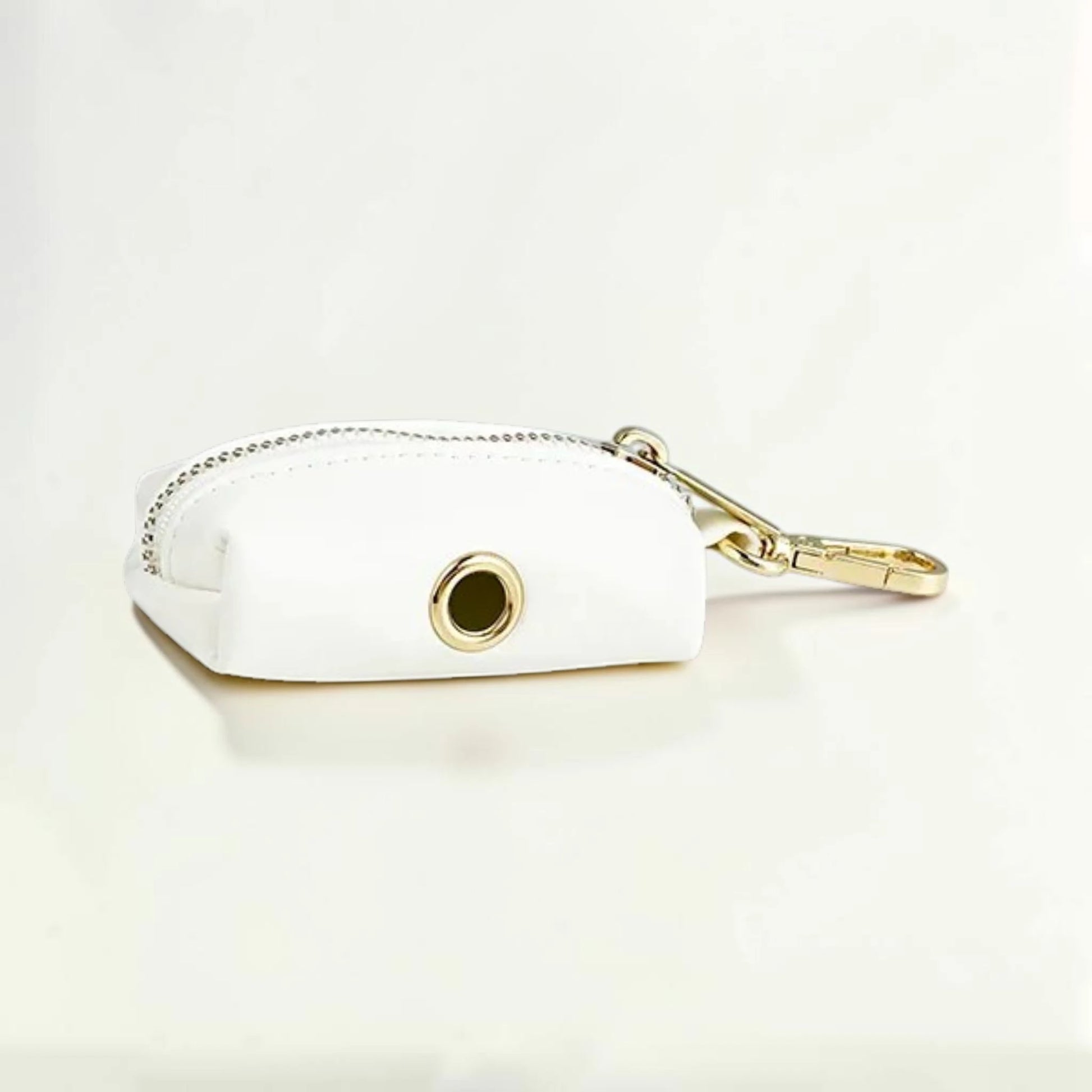 White faux leather dog poop bag holder with gold zip and clip on a light beige background