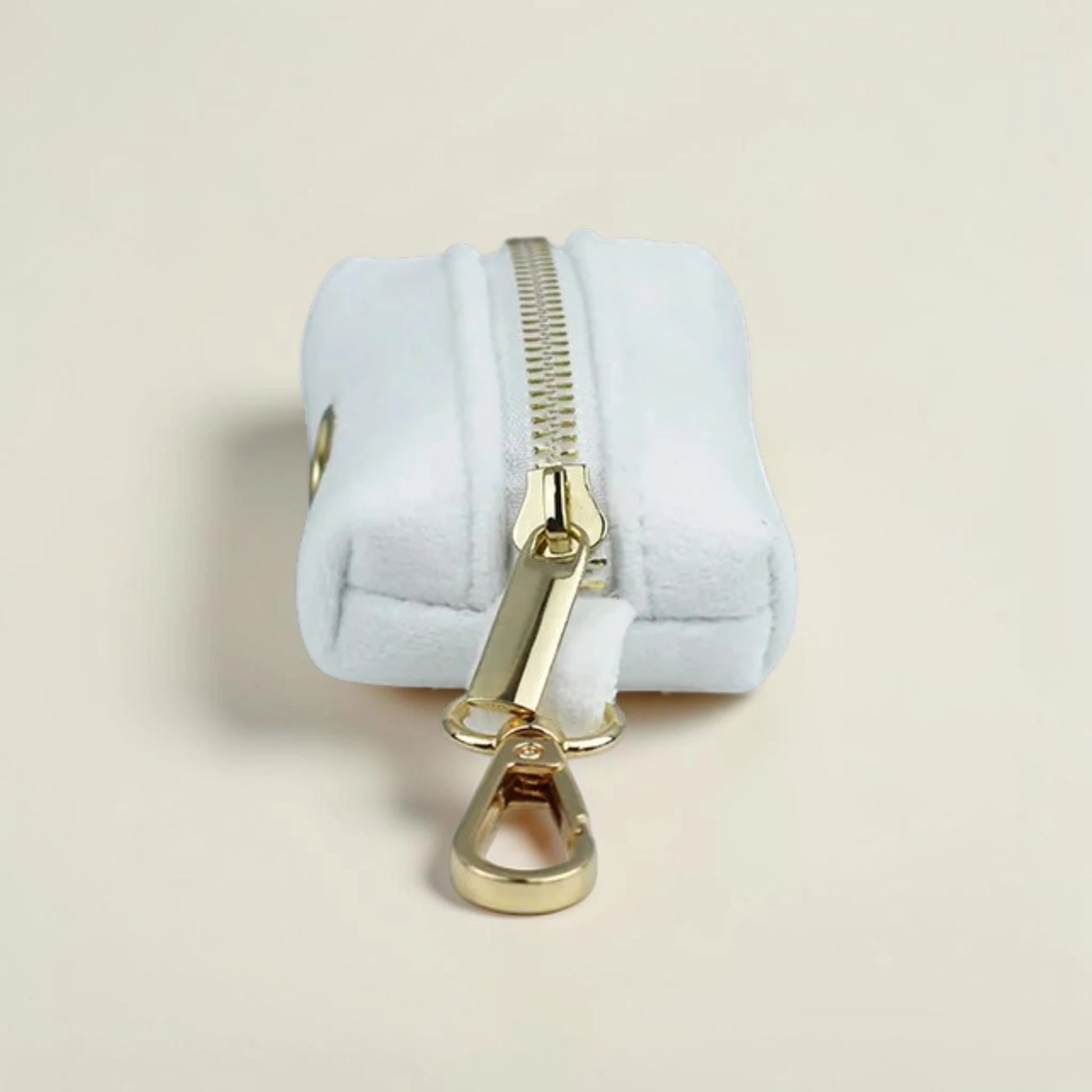 Velvet white dog poop bag holder with gold zip on a beige background
